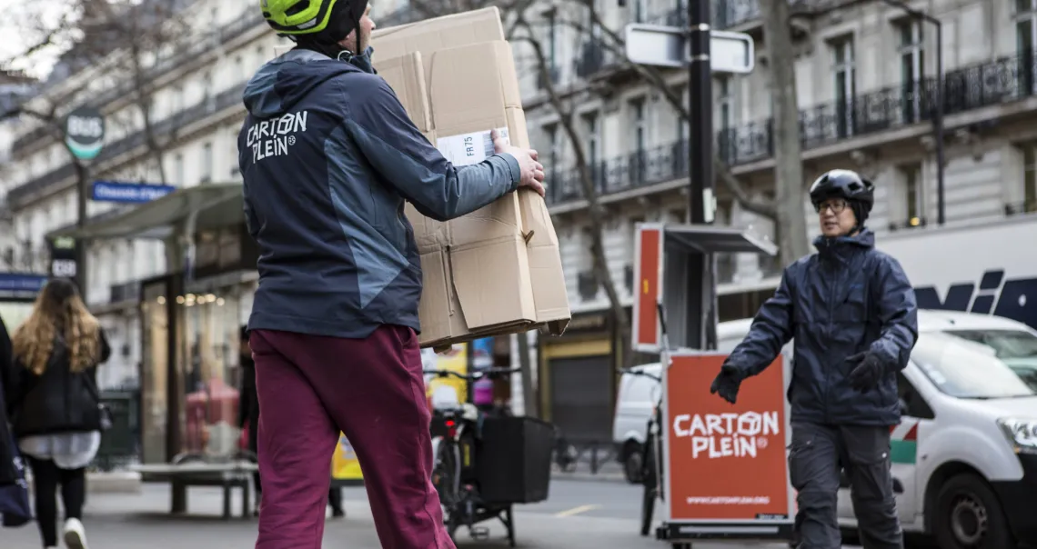 Deux salariés de Carton Plein transportant des cartons dans une rue parisienne 