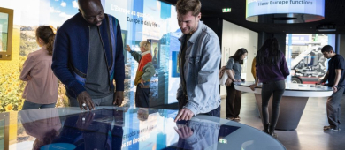 Des jeunes hommes visitent Europa Experience et touchent des écrans sur lesquels est expliqué le fonctionnement des institutions européennes